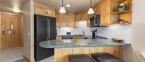 A kitchen with wooden cabinets, a black refrigerator, a granite countertop, and two bar stools.