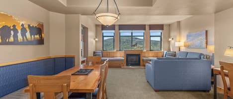 A spacious living area with a wooden dining table, blue cushioned seating, a sofa, and a fireplace.