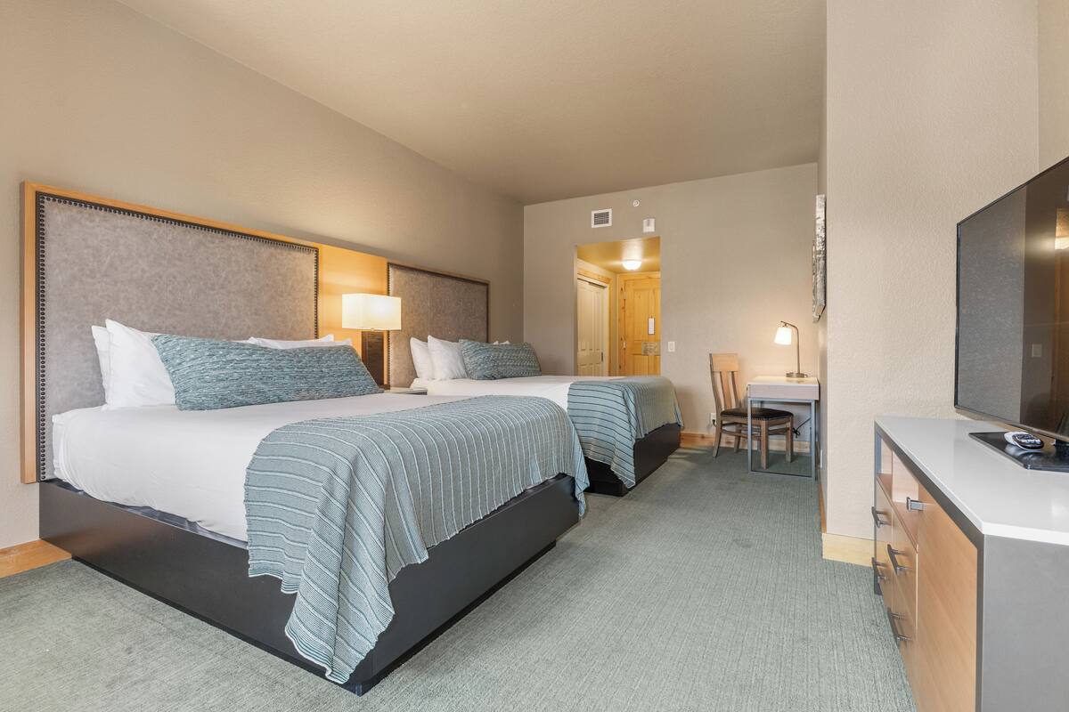 A hotel room with two beds, a desk, a chair, and a TV.