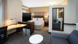 Une chambre d’hôtel comprenant un lit, un bureau avec une télévision, une petite table, un canapé et un miroir.