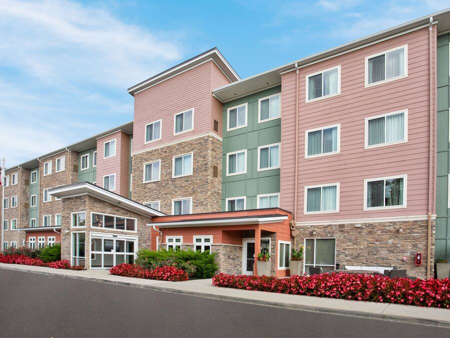 A multi-story hotel with a stone facade, multiple windows, and a landscaped entrance with red flowers.