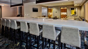 A hotel room with a long dining table, multiple bar stools, a television mounted on the wall, and a kitchen area visible through an open doorway. - Residence Inn by Marriott Columbus Dublin (Dublin)