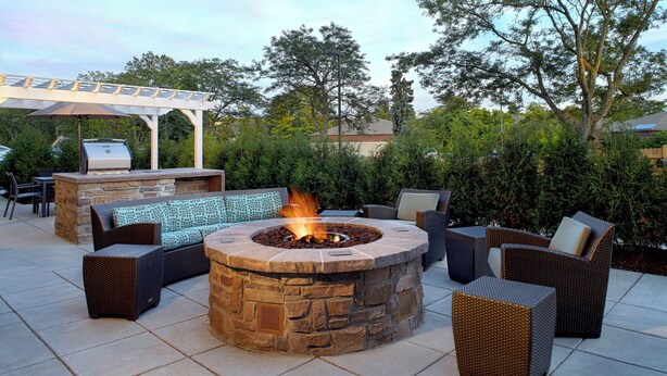 Une terrasse extérieure avec un foyer en pierre, des meubles en osier et un barbecue.
