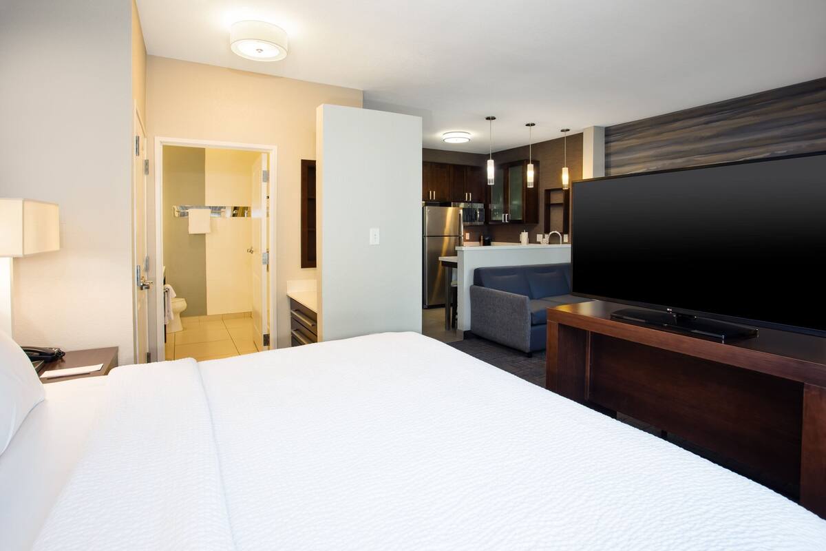 Hotellihuone, jossa on suuri sänky, televisio, työpöytä ja pieni keittiönurkkaus.
