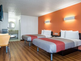 Habitación de hotel con dos camas, un escritorio, un espejo y un baño.