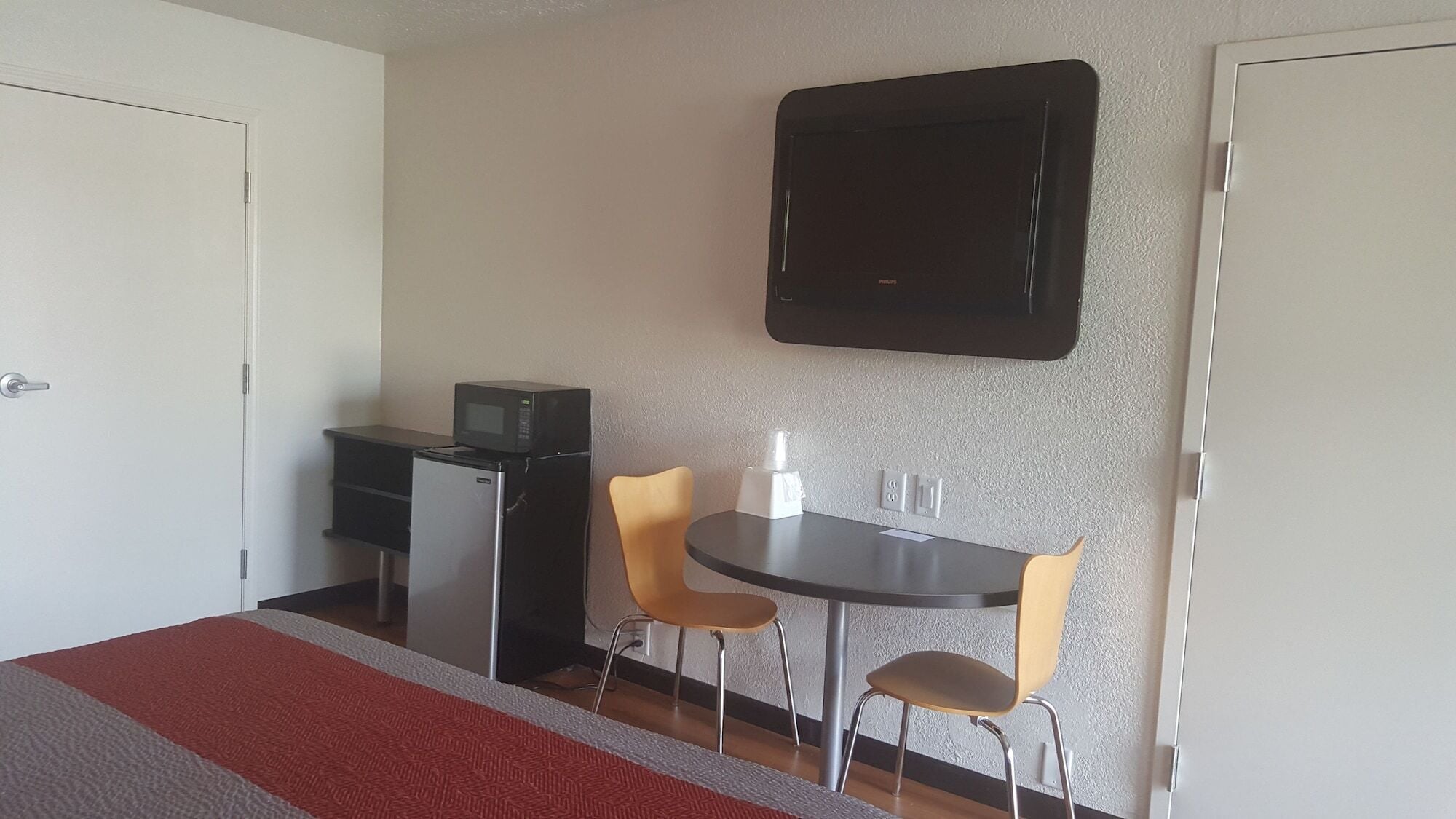 Une petite pièce comprenant un lit, un bureau avec un four à micro-ondes, deux chaises, une table et un téléviseur fixé au mur.