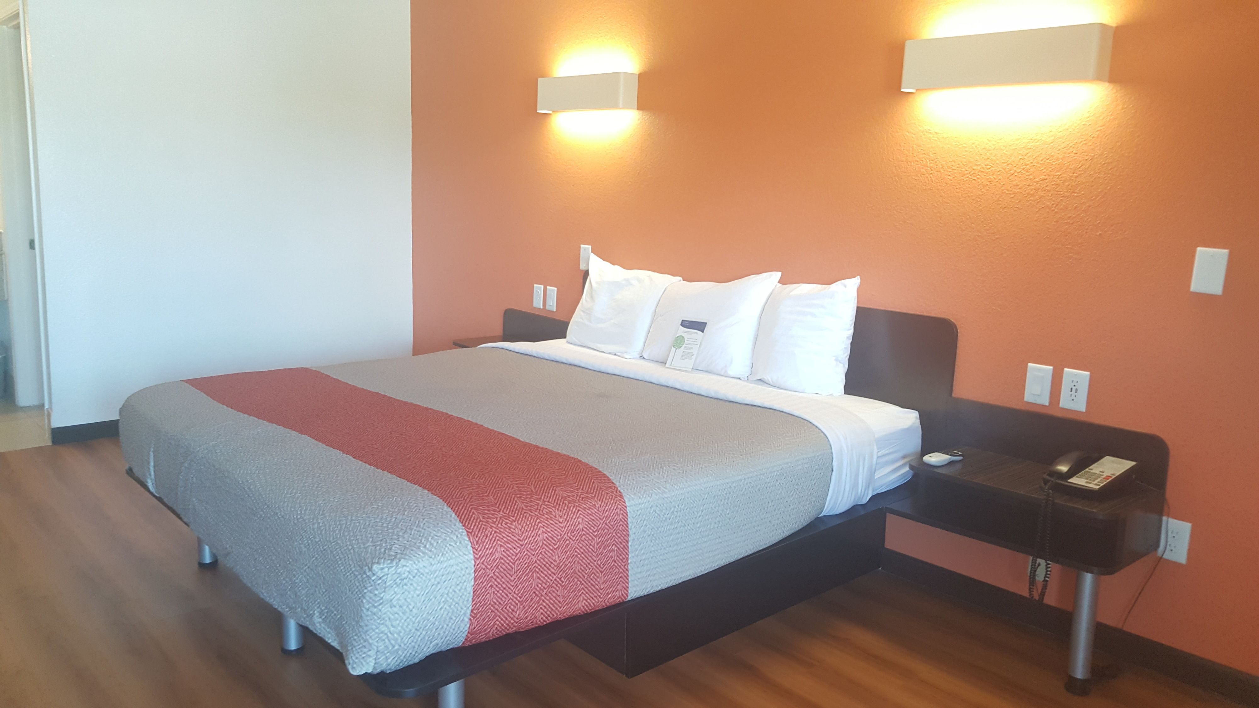 A hotel room with a bed, bedside tables, and wall-mounted lights.