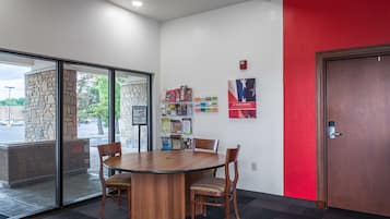 A conference room with a round table and four chairs, a stone pillar, a glass door, a red wall, and a door with a keypad lock.