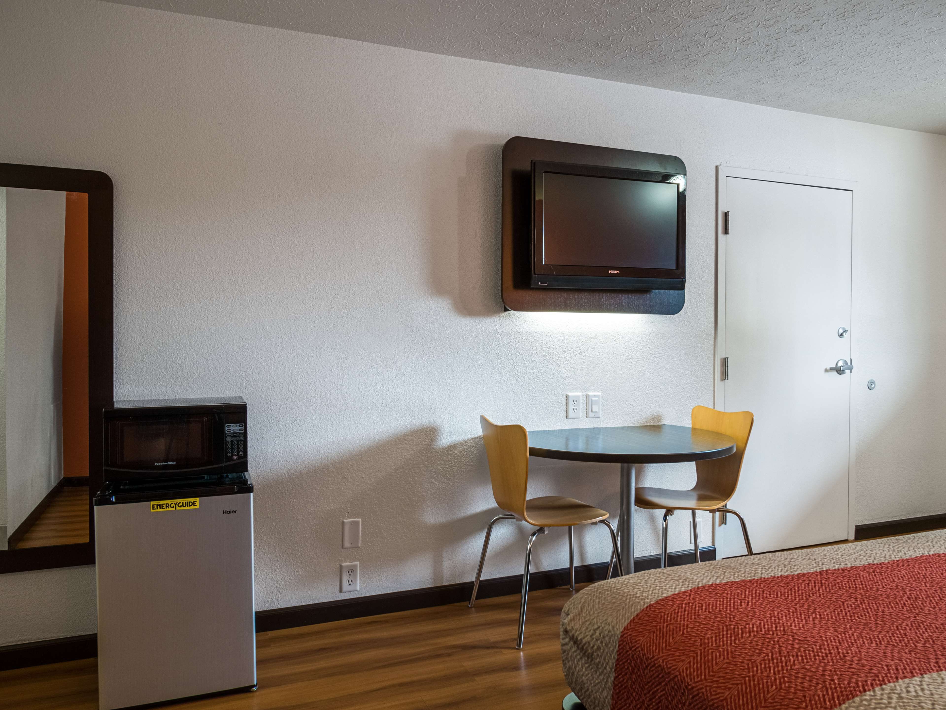 A hotel room with a bed, a microwave, a TV, and two chairs.