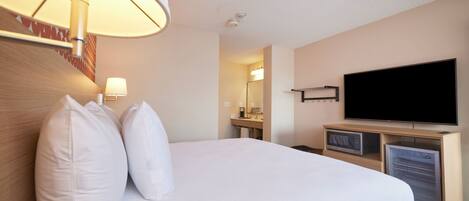 A hotel room with a large bed, a flat-screen TV, a microwave, and a refrigerator.