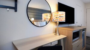 A modern hotel room with a round mirror, a flat-screen TV, a wooden desk, and a built-in microwave. - Olentangy Motor Inn (Columbus)