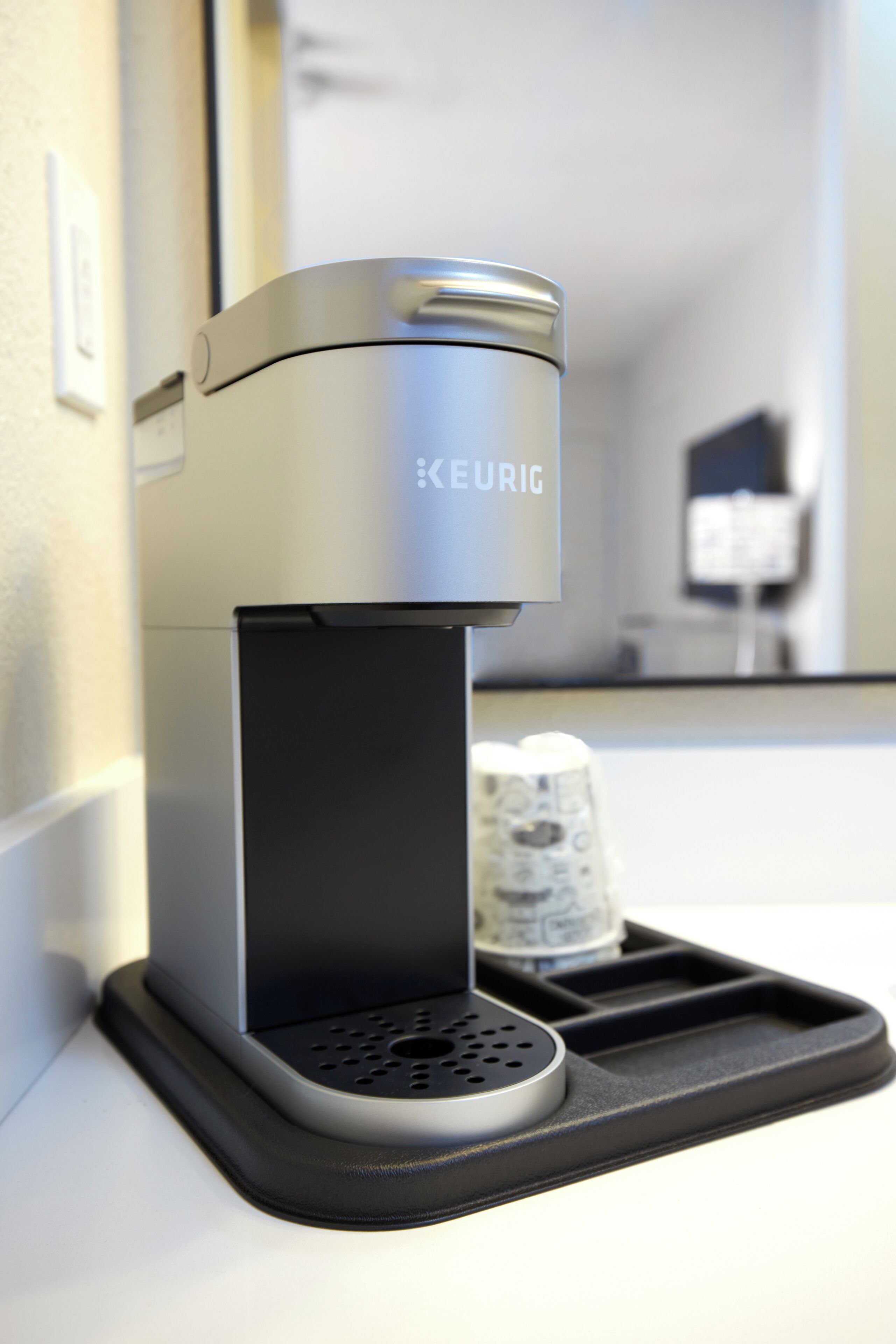 A sleek, modern coffee machine branded 'KEURIG' mounted on a wall with a black tray beneath it.