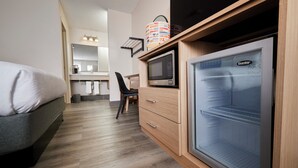 A compact room with a bed, a microwave, a refrigerator, a chair, and a small table with a lamp. - Olentangy Motor Inn (Columbus)