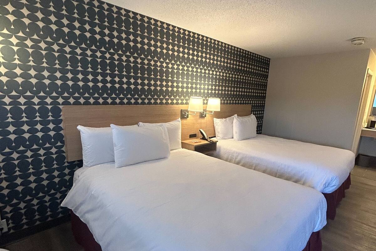 Une chambre d’hôtel avec deux lits, un mur décoré de motifs et une table de chevet avec des lampes.