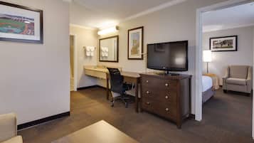 A hotel room with a bed, a desk, a chair, a TV, a dresser, and a bathroom with a mirror and towel rack.