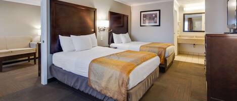 A hotel room with two beds, a sofa, a desk, a mirror, and a bathroom.