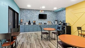 A modern kitchen with blue and yellow walls, a flat-screen TV, and a variety of appliances. - Super 8 by Wyndham Vandalia/Dayton International Airport (Vandalia)