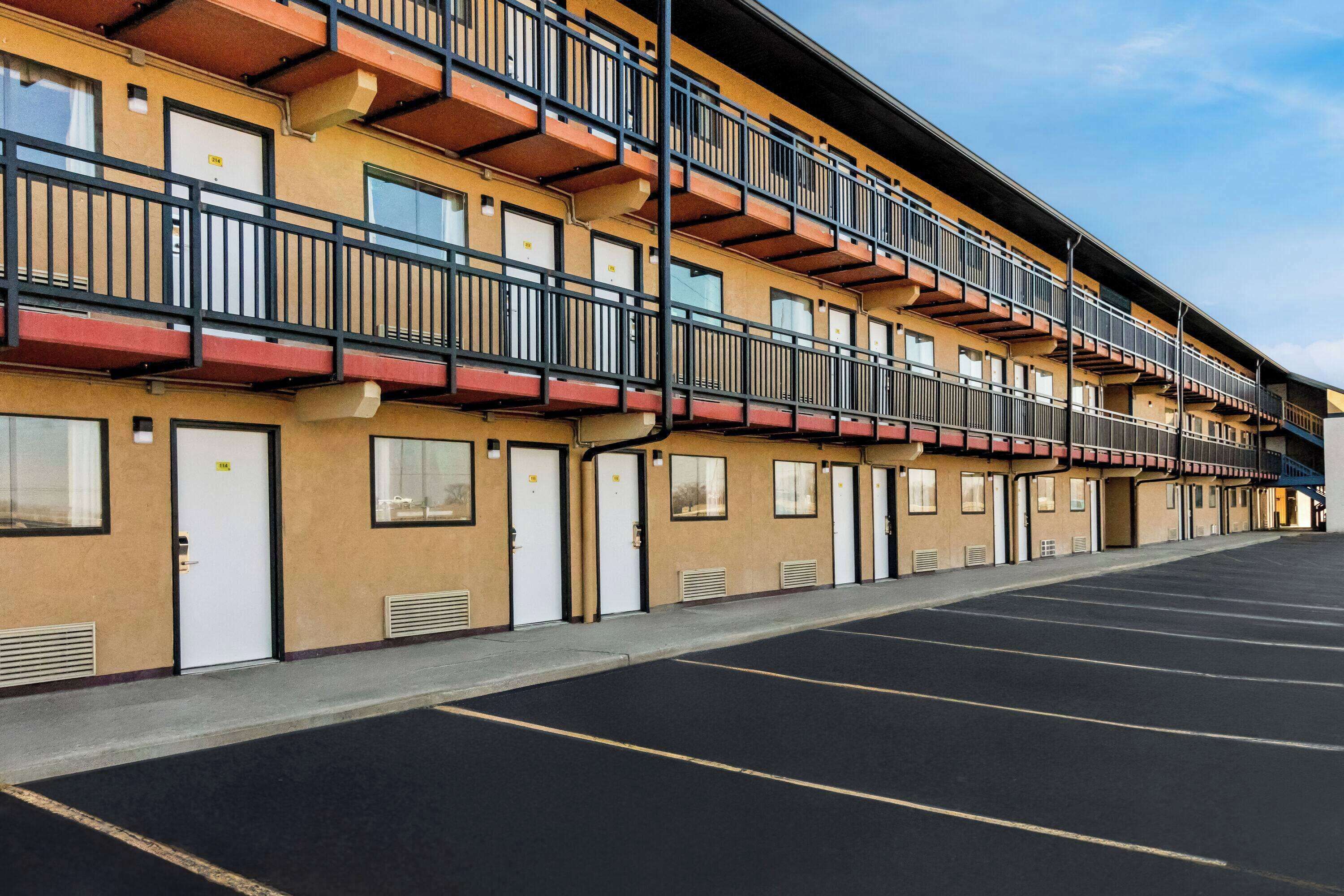 A multi-story hotel with balconies, a parking lot, and a clear sky.