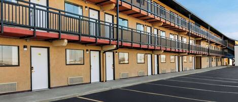 A multi-story hotel with balconies, a parking lot, and a clear sky.