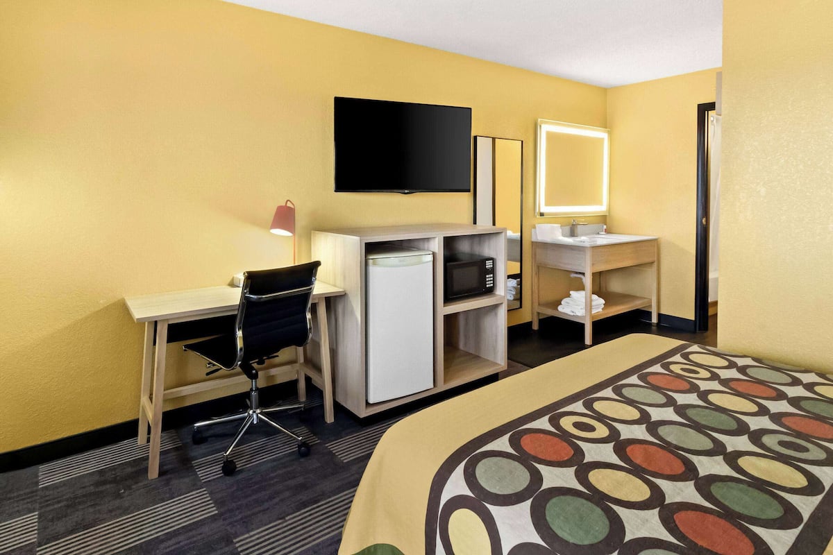 A hotel room with a desk, chair, television, microwave, and a bed with a patterned bedspread.