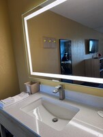 Un baño de hotel con un espejo grande, un lavamanos y un perchero para toallas.