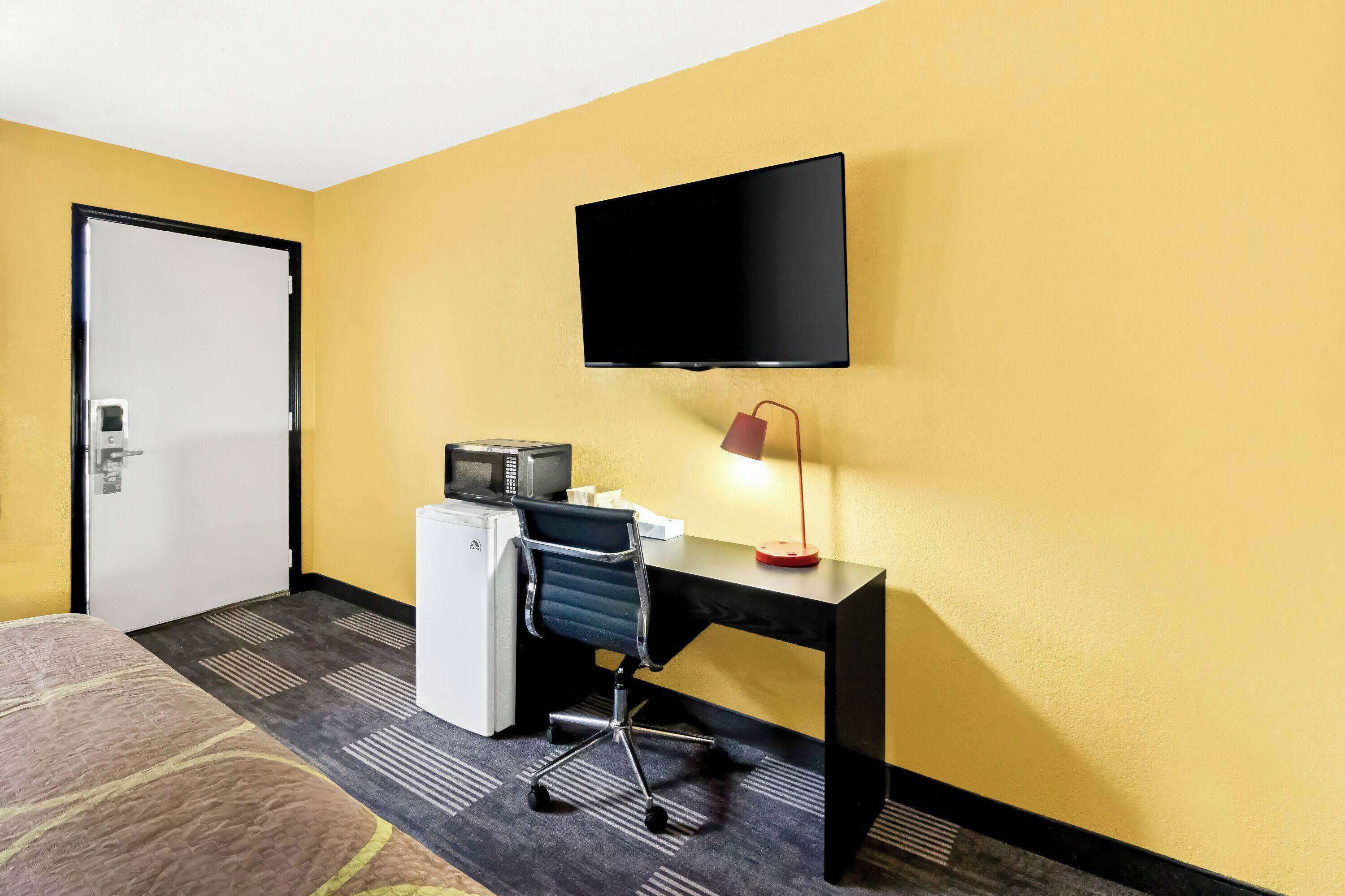 Ein Hotelzimmer mit einem Bett, einem Schreibtisch mit Computer, einem Fernseher und einer Mikrowelle.