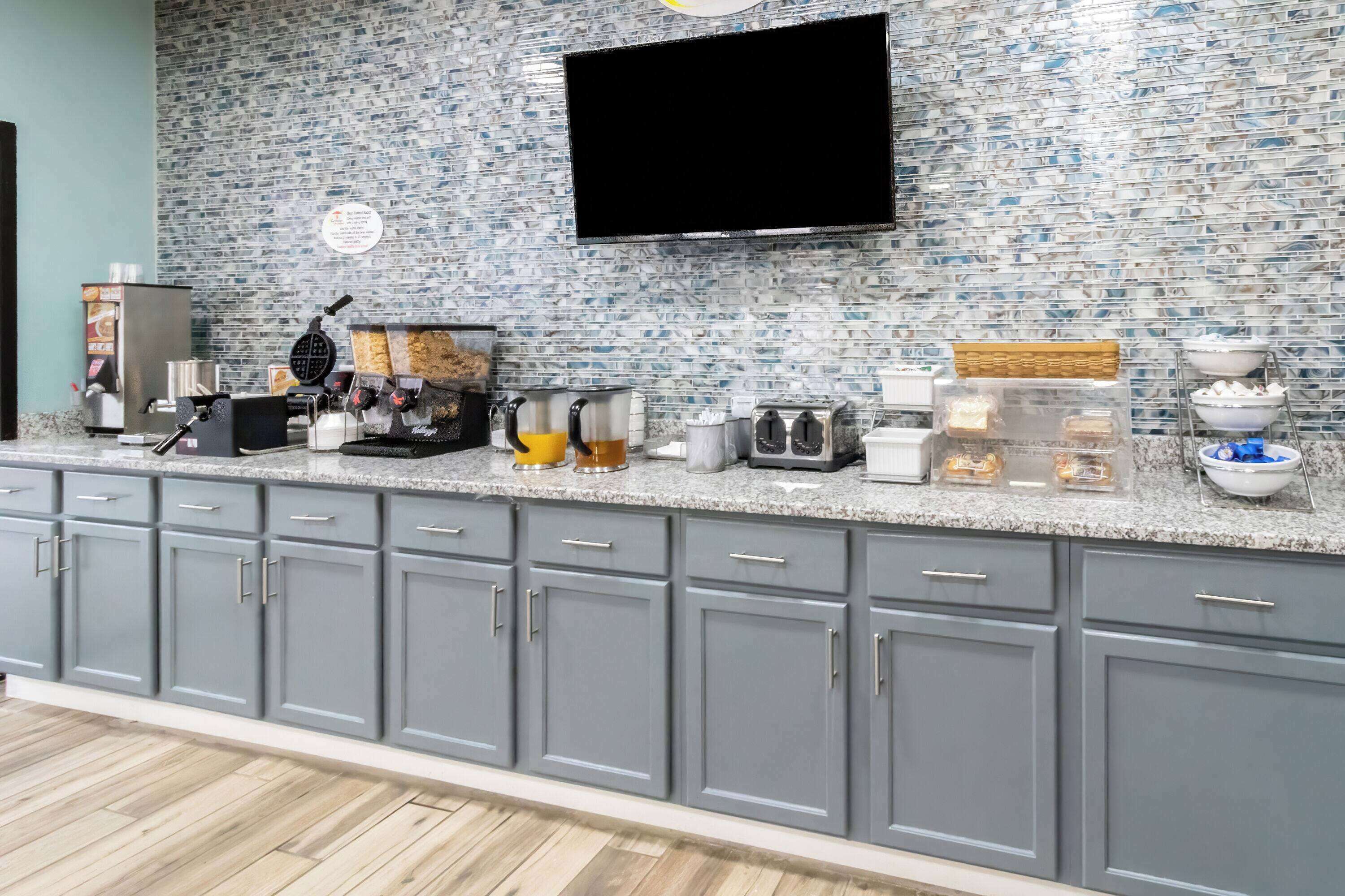 A kitchen with grey cabinets, a tiled backsplash, a flat-screen TV, and various appliances.