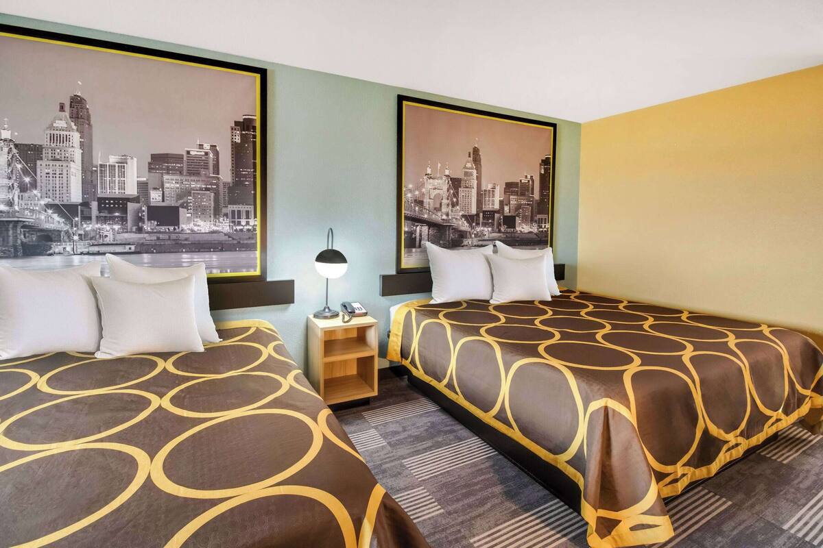 A hotel room with two beds, a nightstand, a lamp, and a cityscape view.