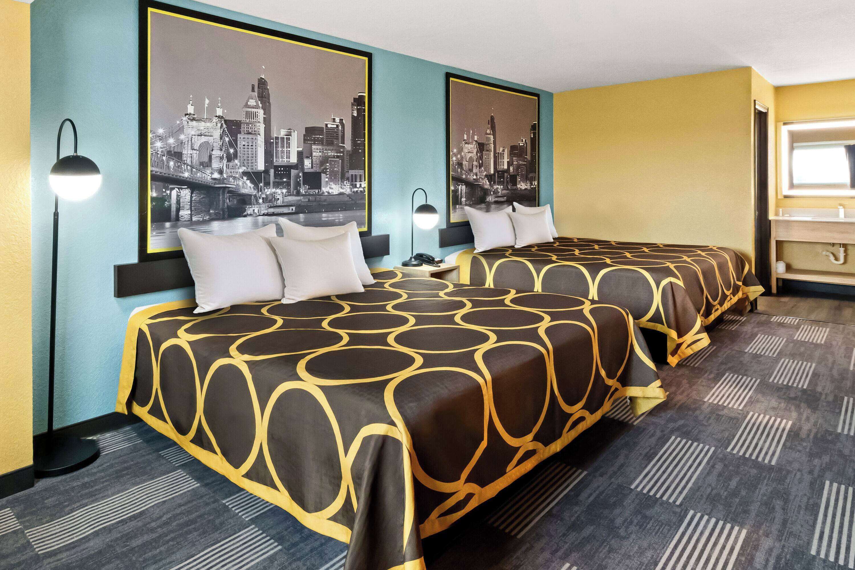 A hotel room with two beds, a cityscape view, a bathroom with a mirror, and a patterned carpet.
