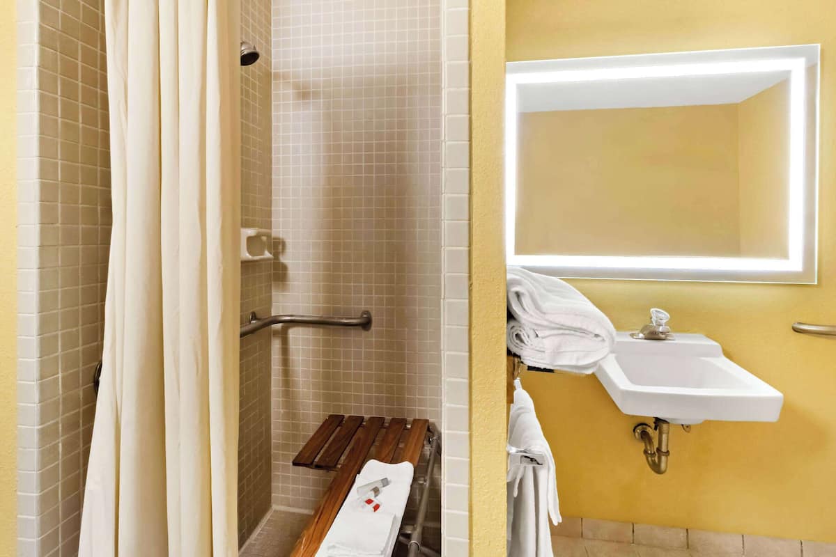 A bathroom with a shower, a sink, a mirror, and a towel rack.