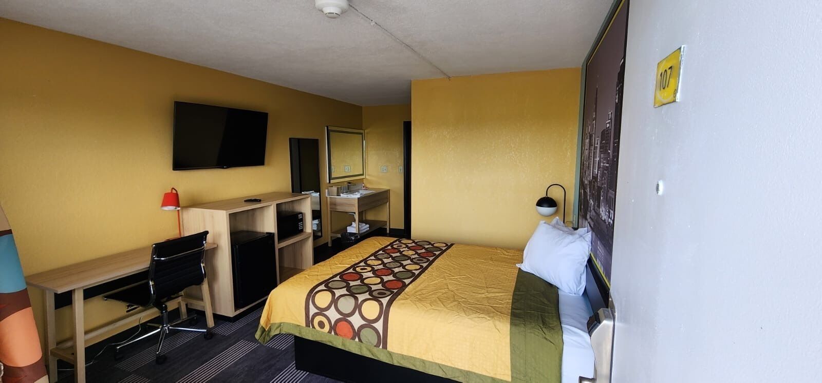 A hotel room with a bed, desk, chair, and a television on the wall.