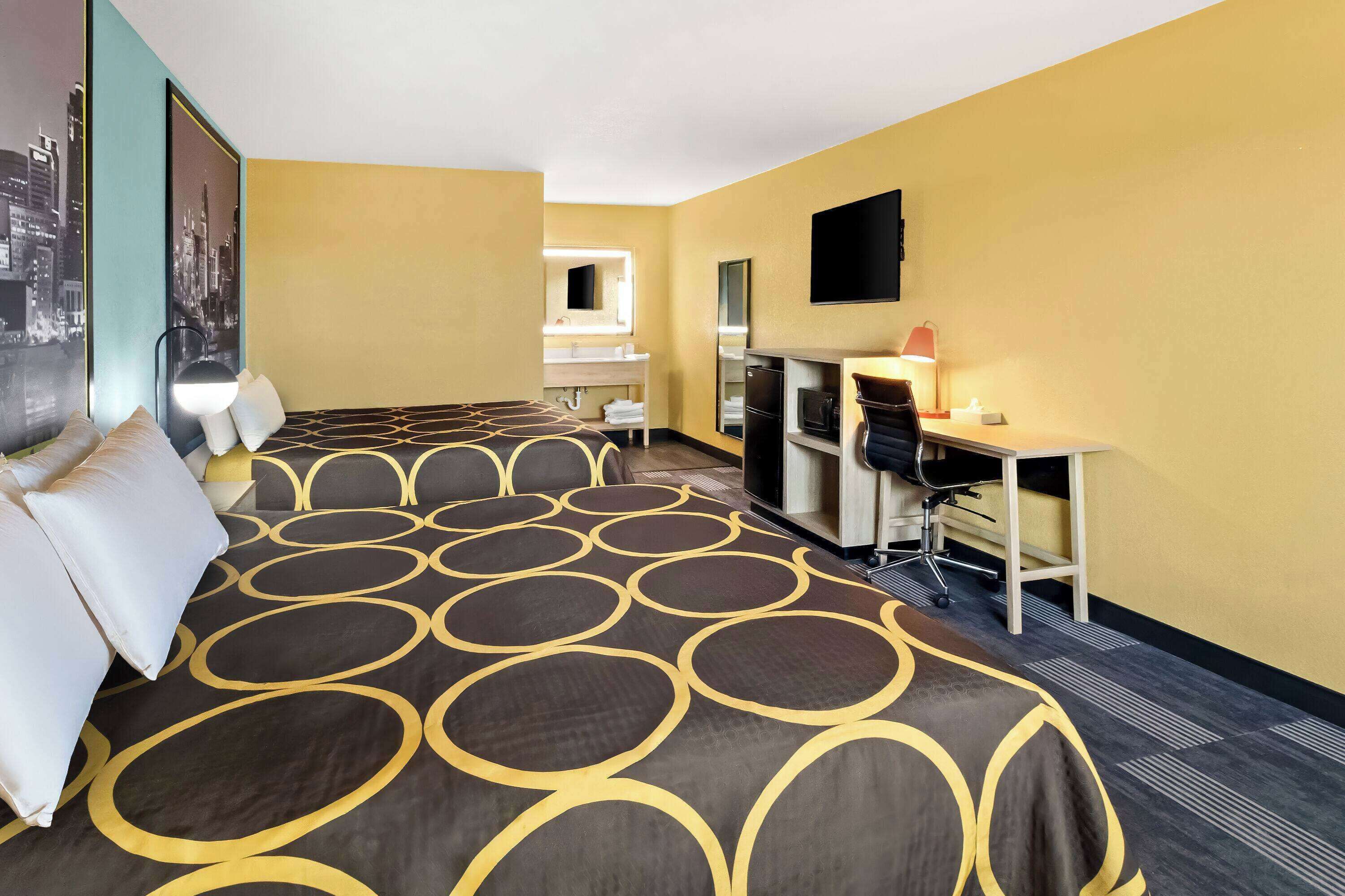 A hotel room with a large bed, a desk, a chair, a television, and a mirror.