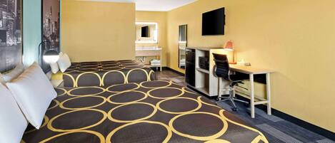 A hotel room with a large bed, a desk, a chair, a television, and a mirror.