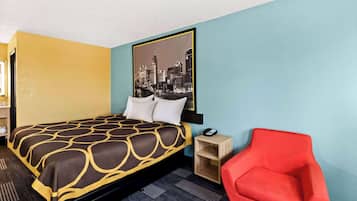 A hotel room with a bed, a red chair, a nightstand, and a cityscape painting on the wall.