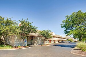 Un motel con fachada de piedra, zona de estacionamiento techada y un cielo azul despejado.