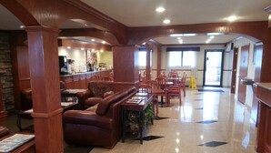 Un hall d’entrée spacieux avec un espace salon central, une cuisine à l’arrière-plan et un sol carrelé orné d’un motif géométrique.