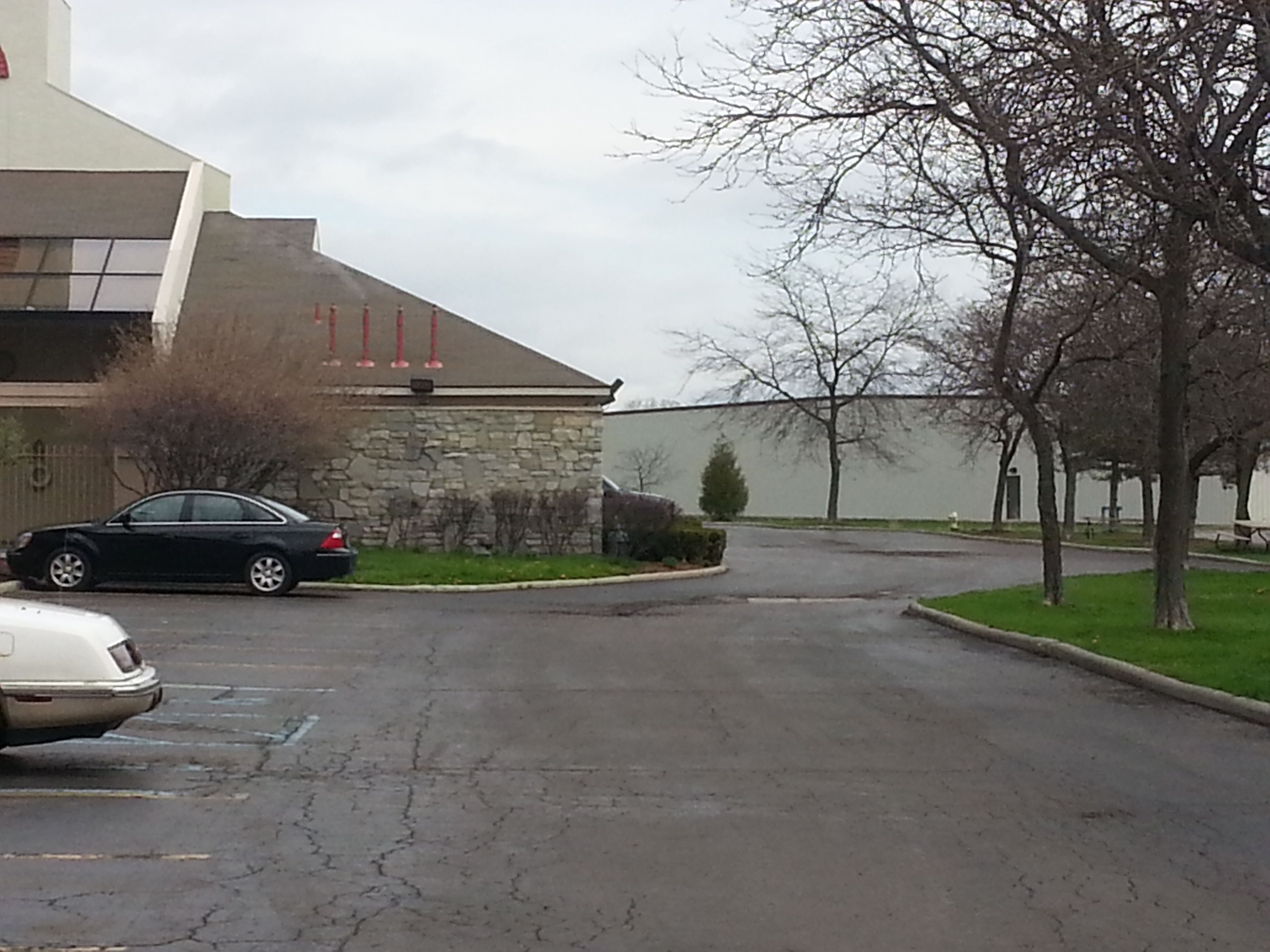 A parking lot with a stone building, a black car, and a white car.