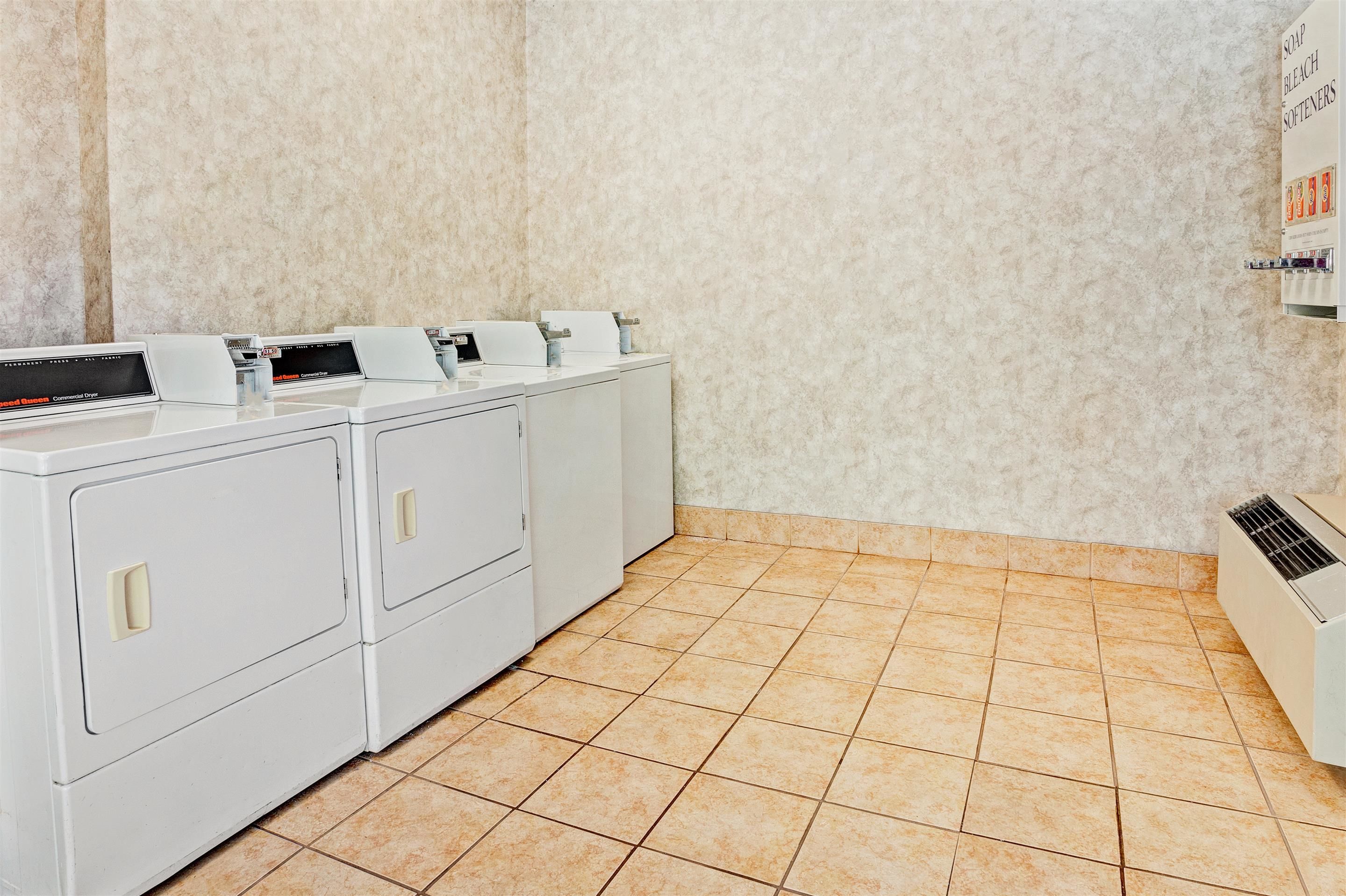 A laundry room with stacked washers and dryers, a tiled floor, and a wall-mounted air conditioning unit.