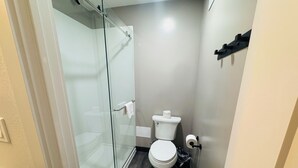 A small bathroom with a glass shower enclosure, a toilet, and a wooden floor. - Motel 6 Southgate, MI - Detroit (Southgate)