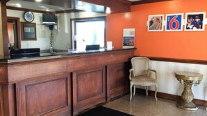 A reception desk with a clock, a television, and a sign for a motel. - Motel 6 Southgate, MI - Detroit (Southgate)