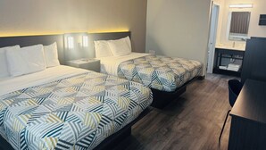 A hotel room with two beds, a desk, a chair, a bathroom with a sink and mirror, and a ceiling light. - Motel 6 Southgate, MI - Detroit (Southgate)