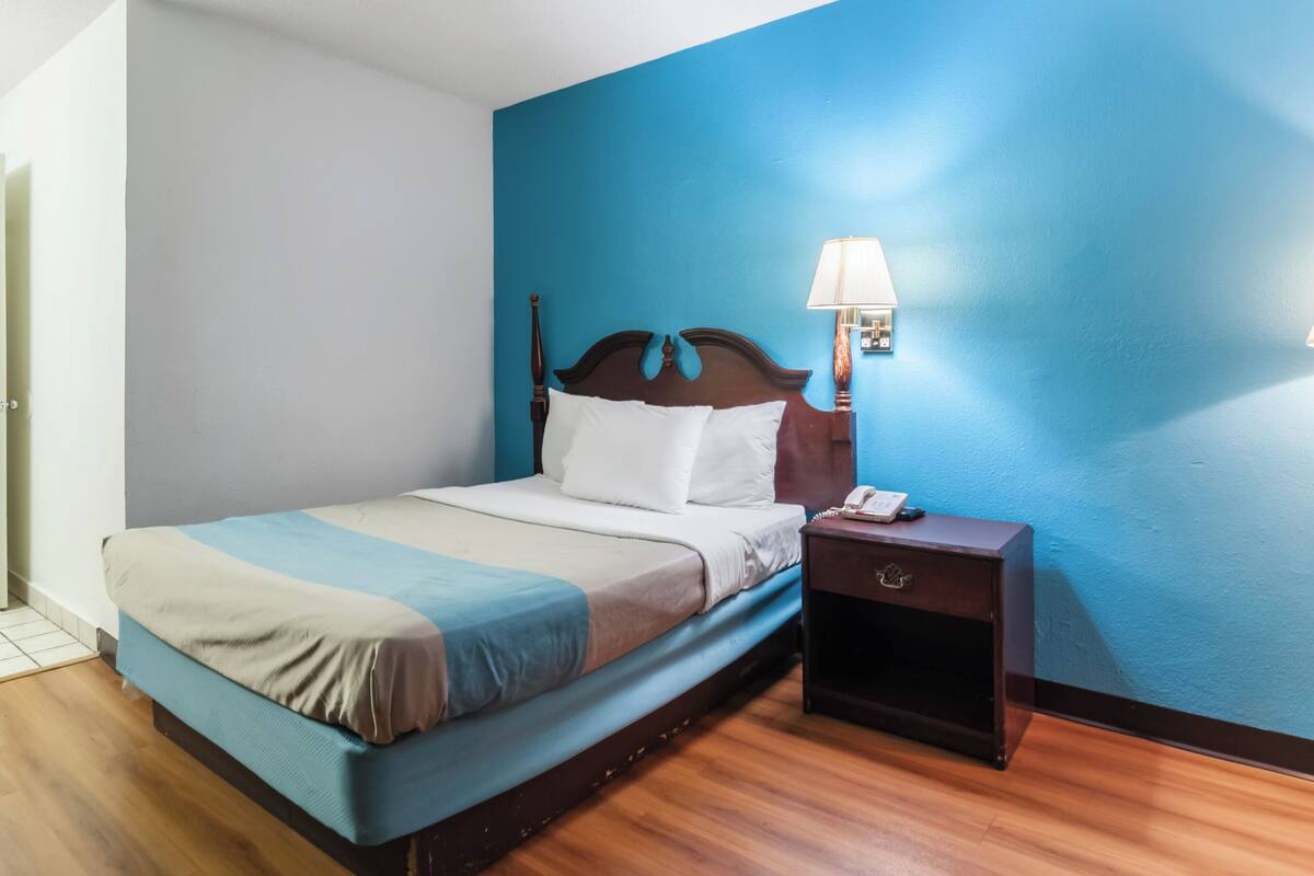 A hotel room with a bed, bedside table, lamp, and a blue accent wall.