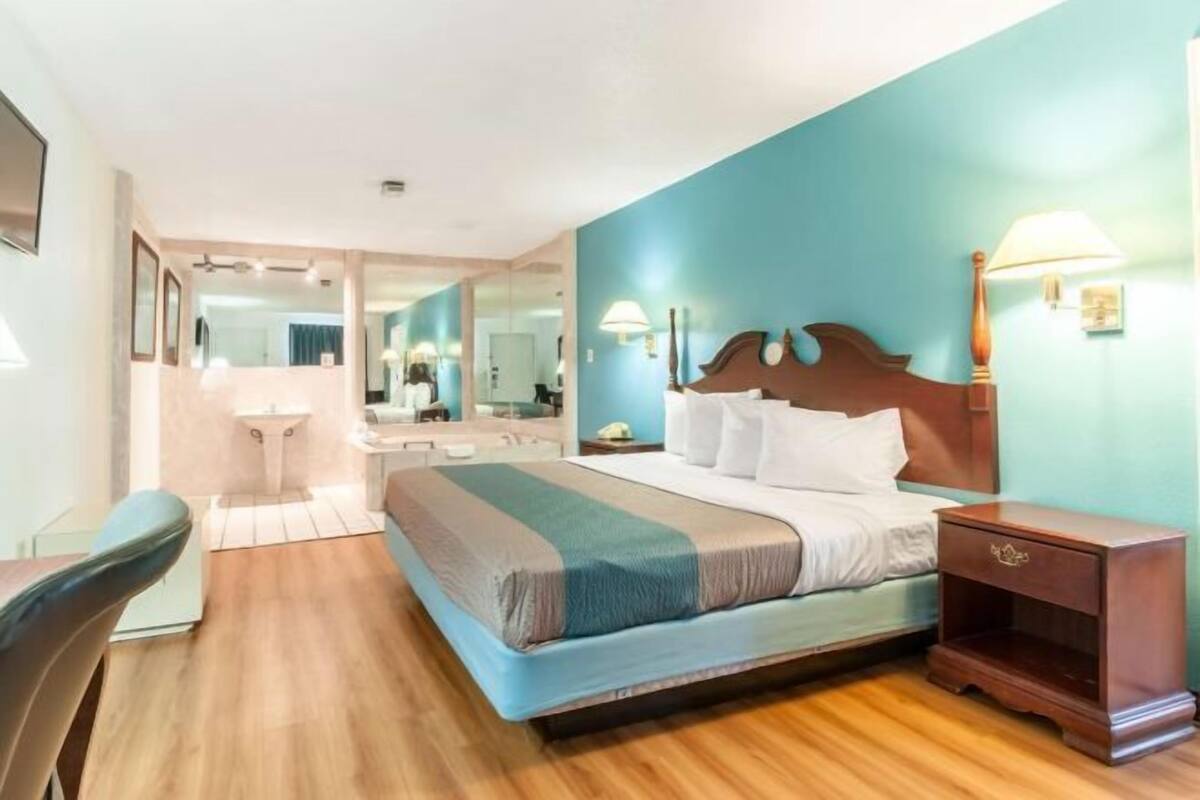 A hotel room with a bed, bedside table, mirror, and a view of the bathroom.