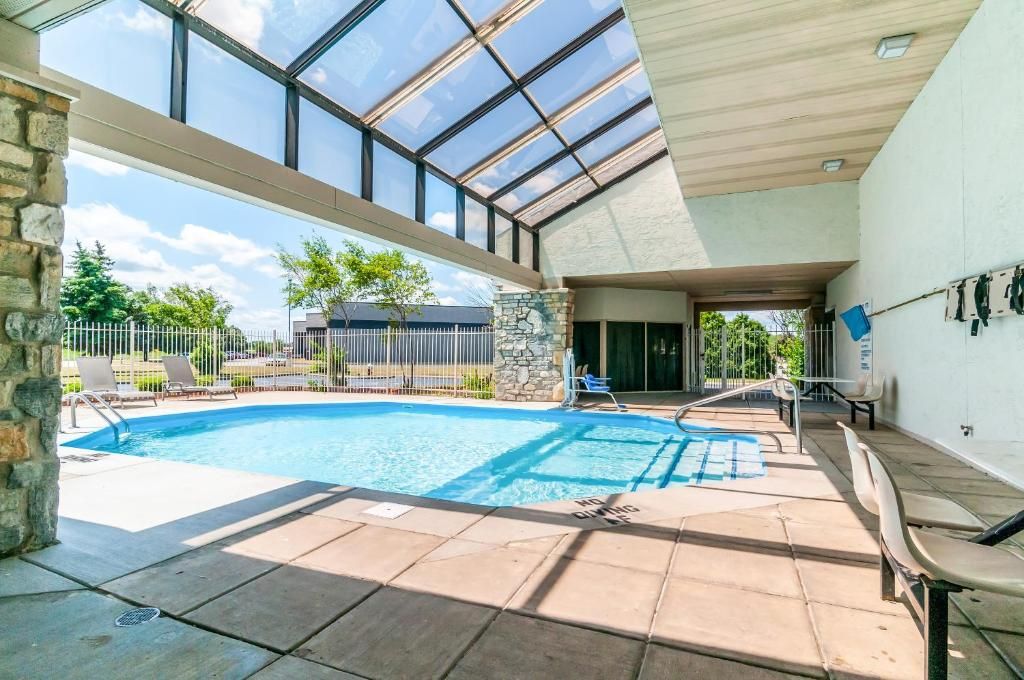 An indoor swimming pool with a glass ceiling, stone pillars, and a patio area with lounge chairs.