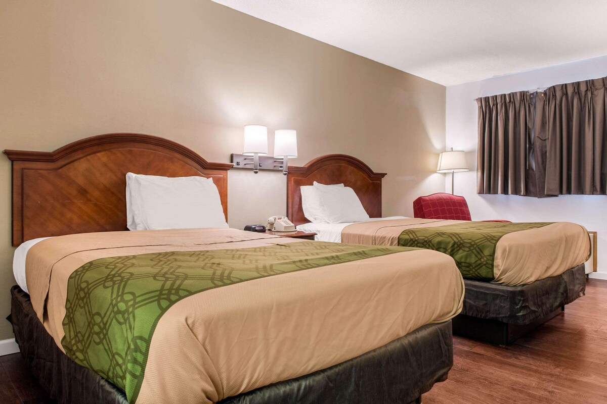 A hotel room with two beds, wooden headboards, bedside lamps, a telephone, and a window with curtains.