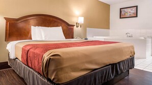 A hotel room with a large bed, a bedside lamp, a bathroom with a bathtub, and a wall-mounted artwork.