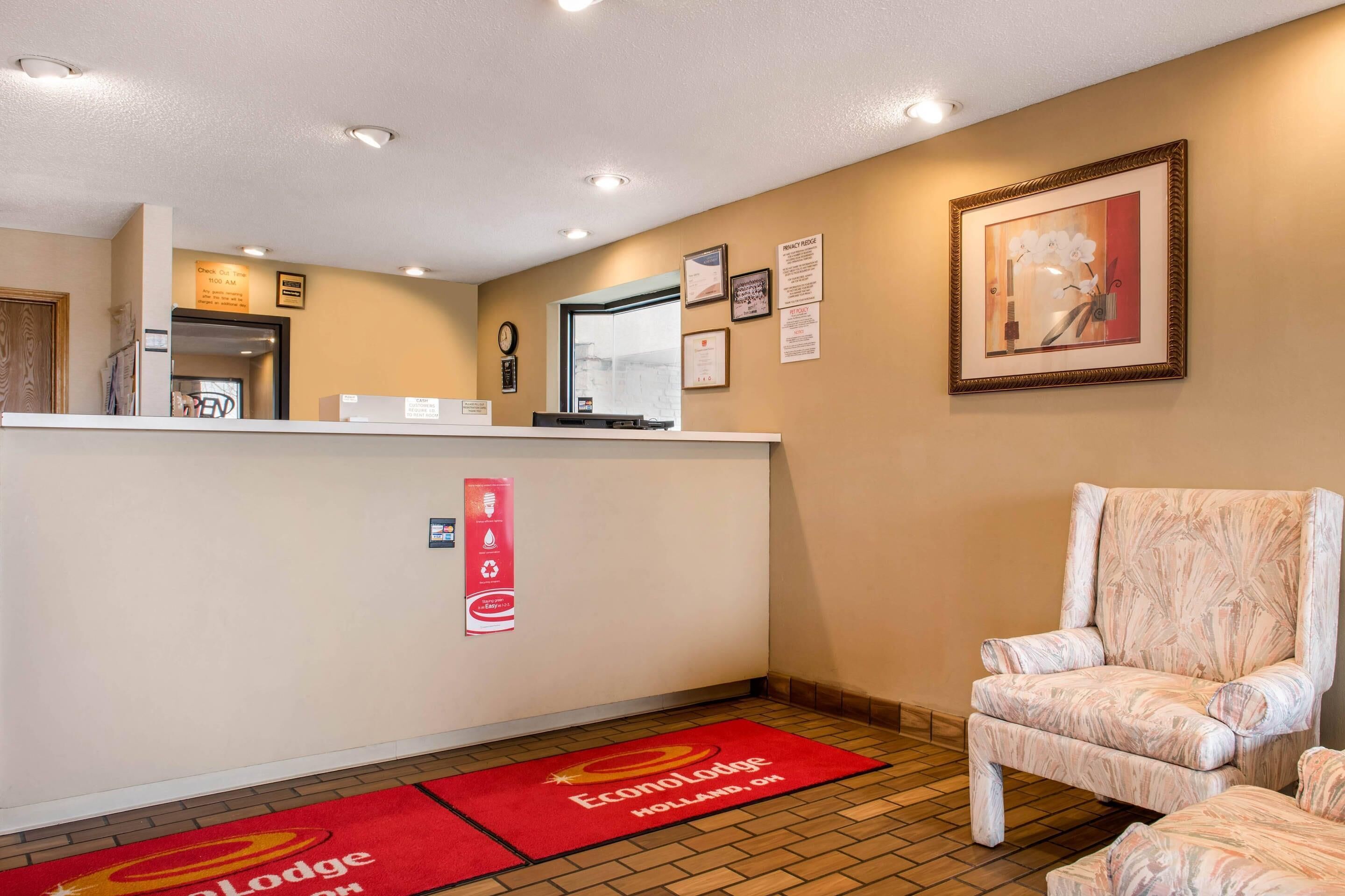 A reception area with a counter, a chair, a framed picture, and a red carpet with text.
