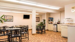 Un espace repas avec des tables et des chaises, une cuisine équipée d’un réfrigérateur et d’une machine à café, et des œuvres d’art accrochées aux murs.