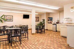 A dining area with tables and chairs, a kitchen with a refrigerator and a coffee machine, and artwork on the walls. - Econo Lodge Holland - Toledo (Holland)