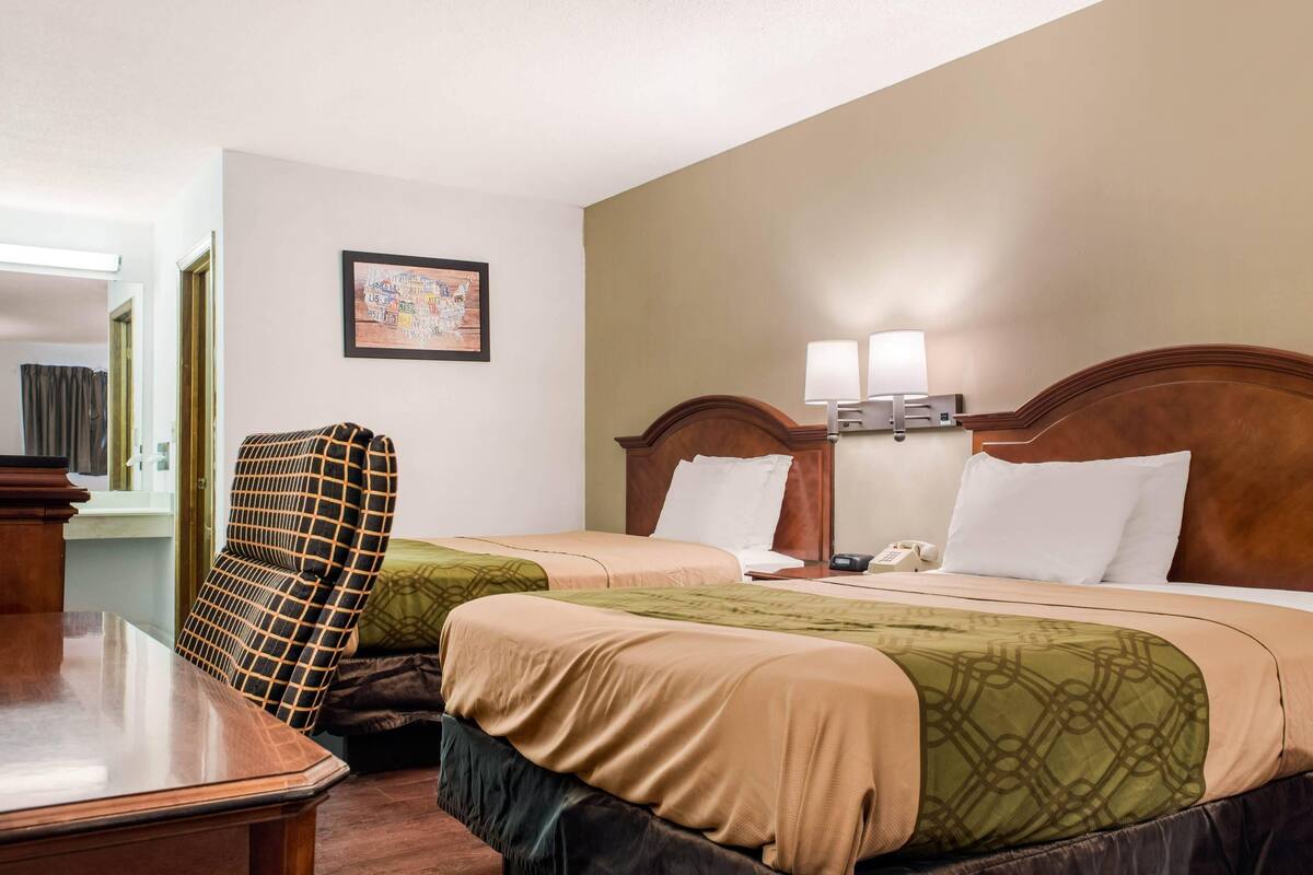 Een hotelkamer met twee bedden, een bureau, een stoel, een lamp en een schilderij aan de muur.